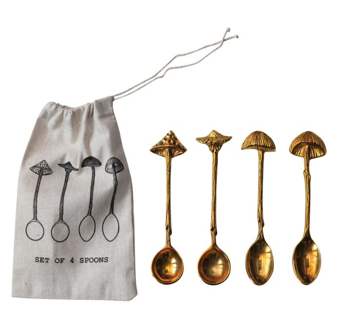 A set of four brass spoons with mushroom-shaped handles, displayed alongside a printed drawstring bag with the illustration of the spoons.