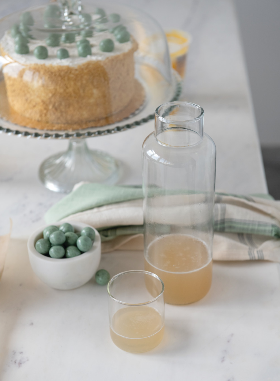 A clear glass decanter with a matching drinking glass, both are empty and set against a white background.