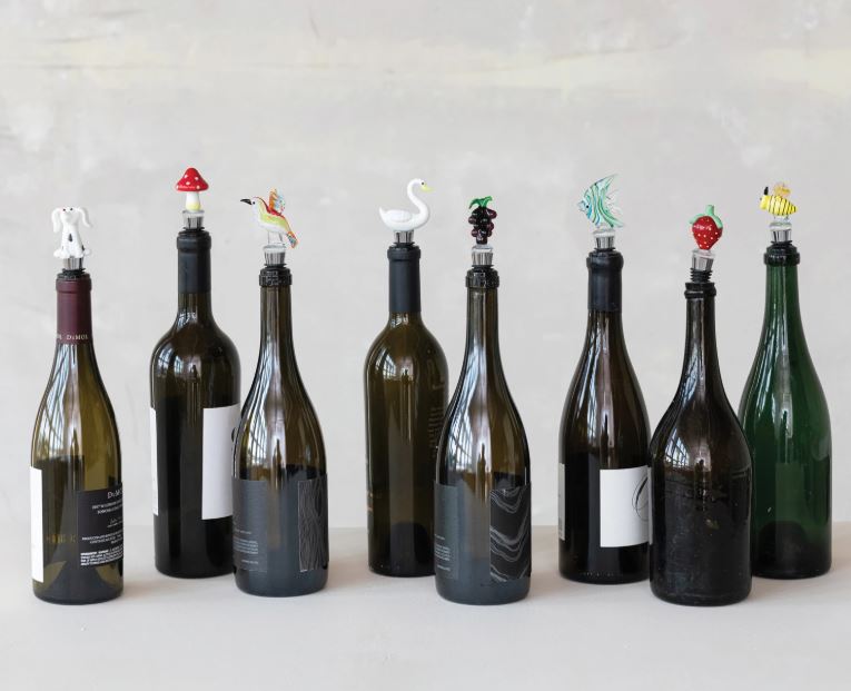 A collection of hand-blown glass bottle stoppers with zinc alloy bases in various colorful designs, displayed on top of a wine bottle.