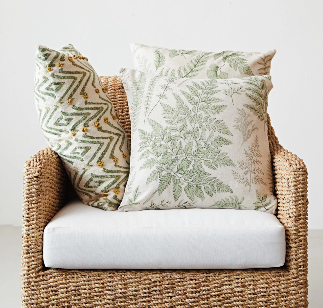 A woven cotton blend lumbar pillow with a geometric floral pattern in natural, green, and mustard colors, featuring French knots.